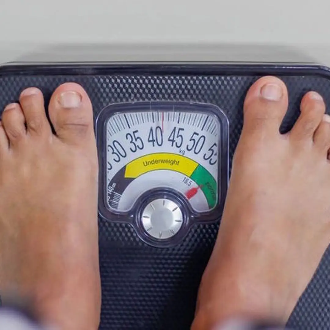 Person standing barefoot on a black analog weighing scale showing a weight of about 47 kilograms in the overweight zone.