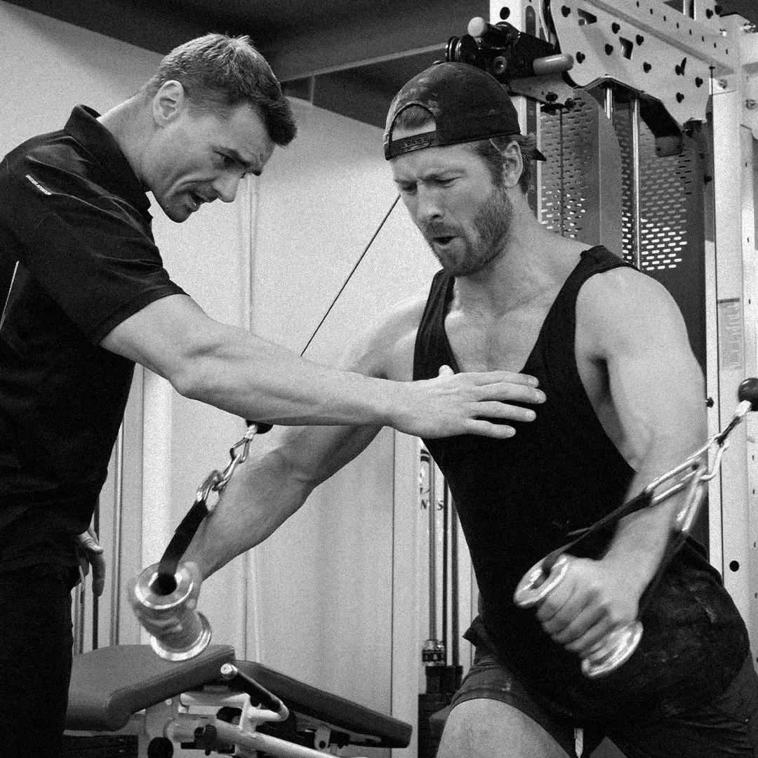 Fitness trainer coaching a man performing cable chest fly exercise in a gym.