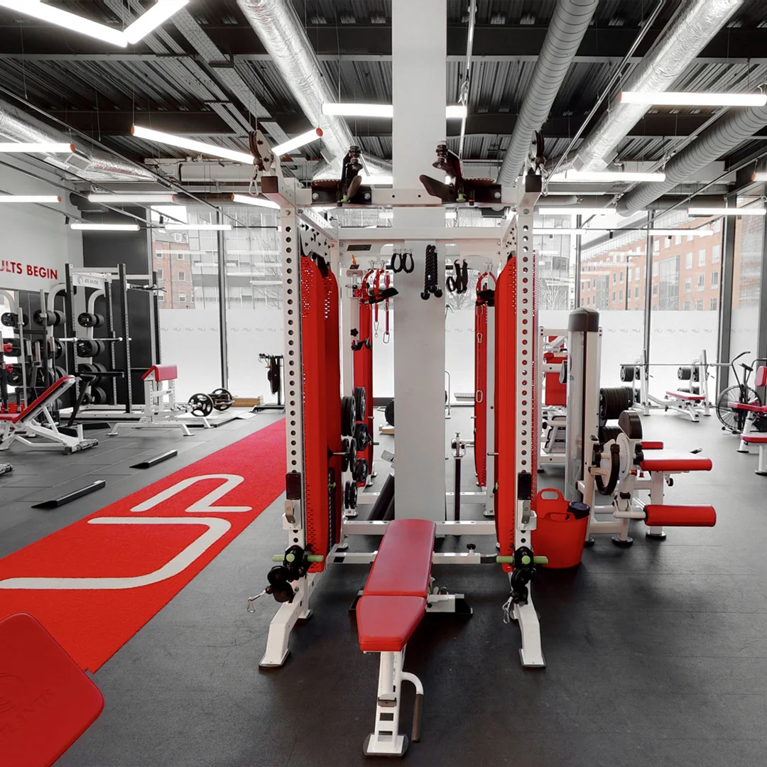 Modern gym interior with red and white weightlifting equipment and large windows showing city buildings.