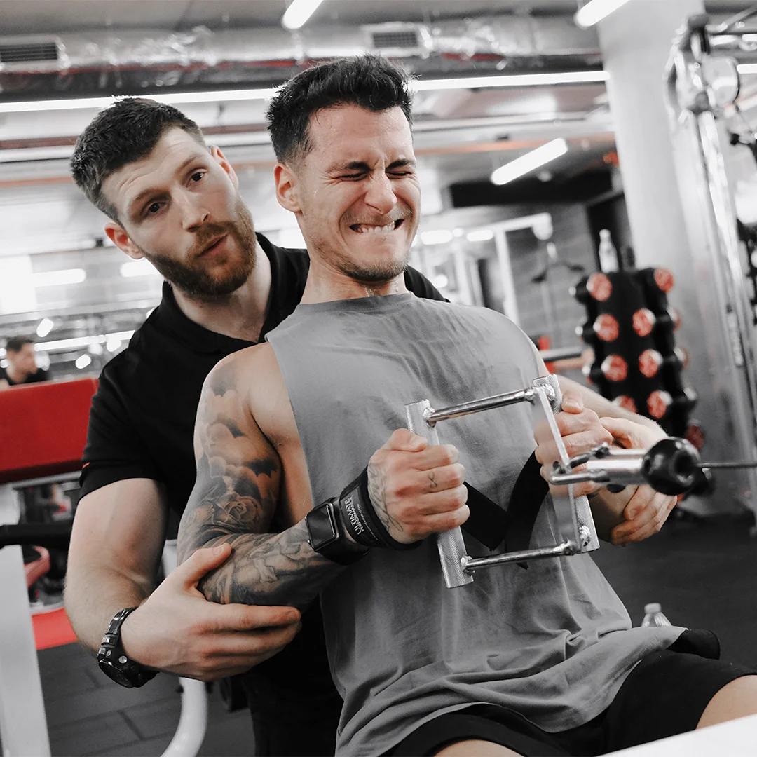 Personal trainer assisting a man lifting weights on a rowing machine in a gym.