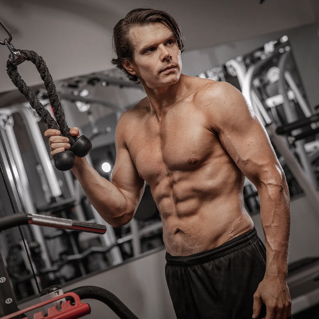Muscular shirtless man working out with a rope attachment in a gym.