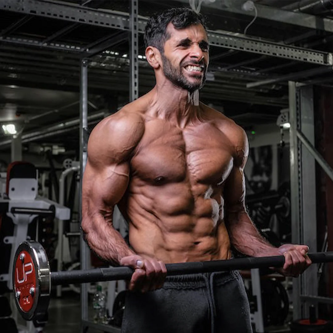 Muscular man lifting a barbell weight in a gym, showing defined chest and arm muscles.