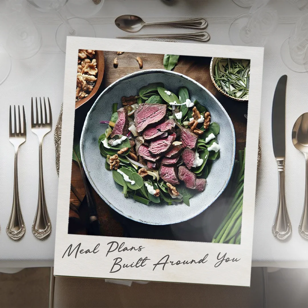 Top-down view of a bowl with sliced medium-rare steak, spinach, walnuts, and a drizzle of white dressing on a wooden table.