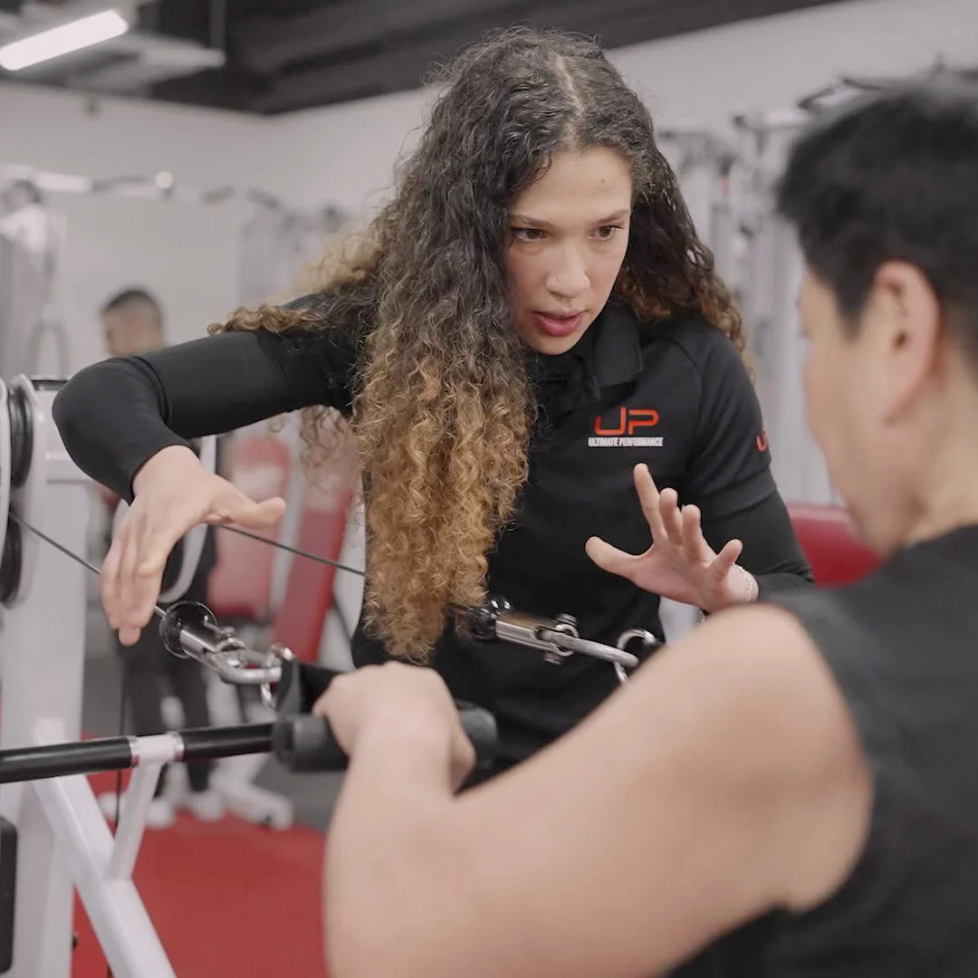 Female fitness trainer instructing a man on cable machine exercise in a gym.