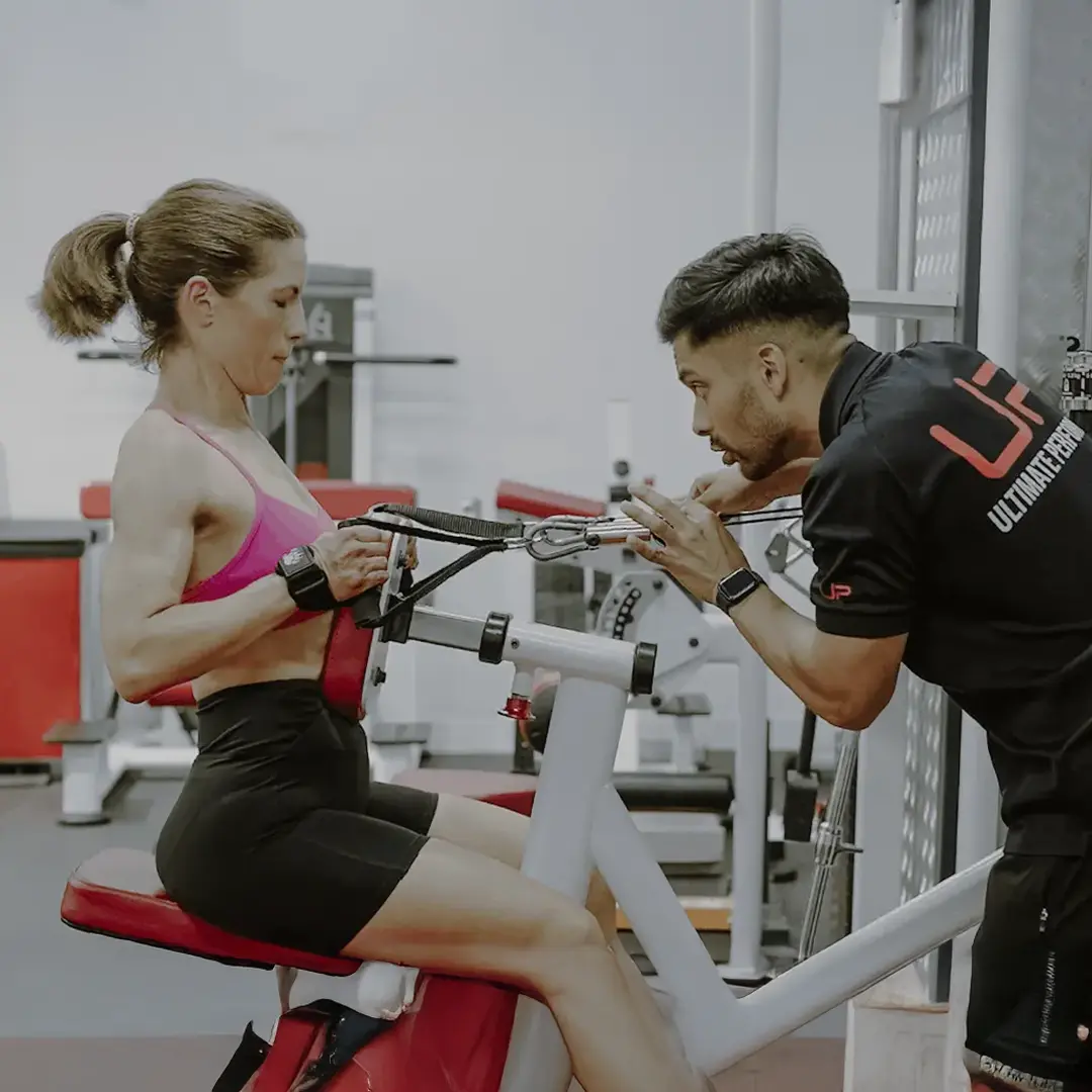 Woman performing seated cable row exercise under guidance of a male personal trainer in a gym.
