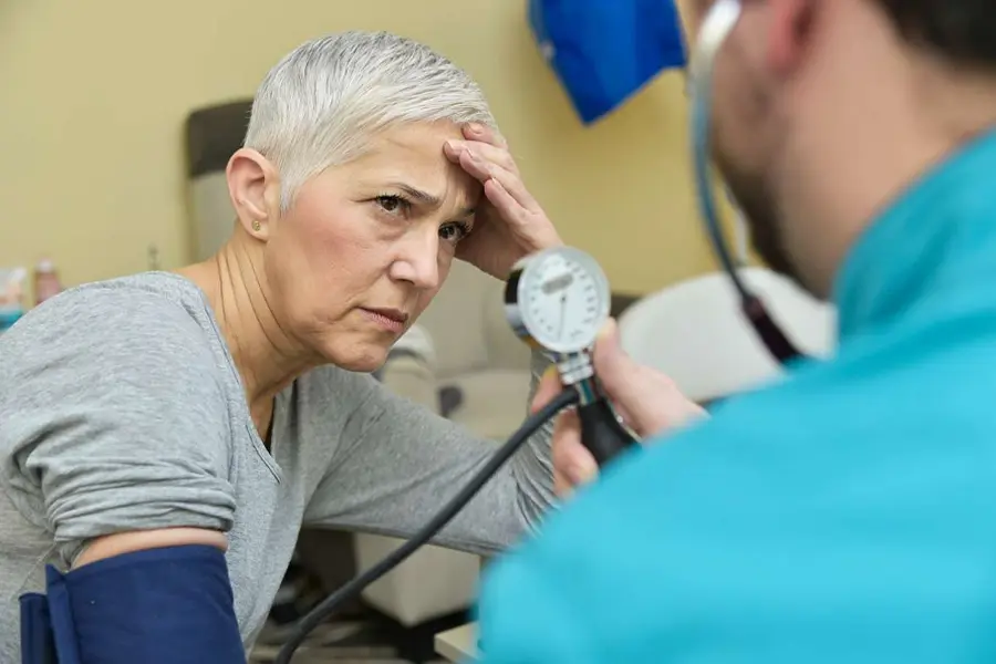 Senior woman with short gray hair looking concerned as a healthcare professional measures her blood pressure.