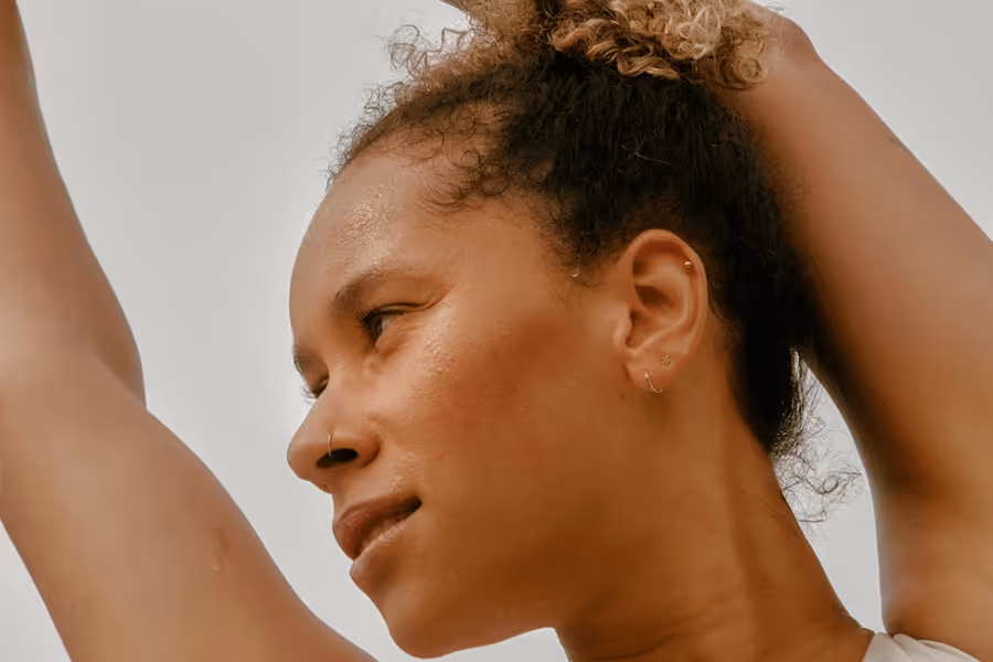 Close-up of a woman with curly hair tied up, looking to the side with arms raised.