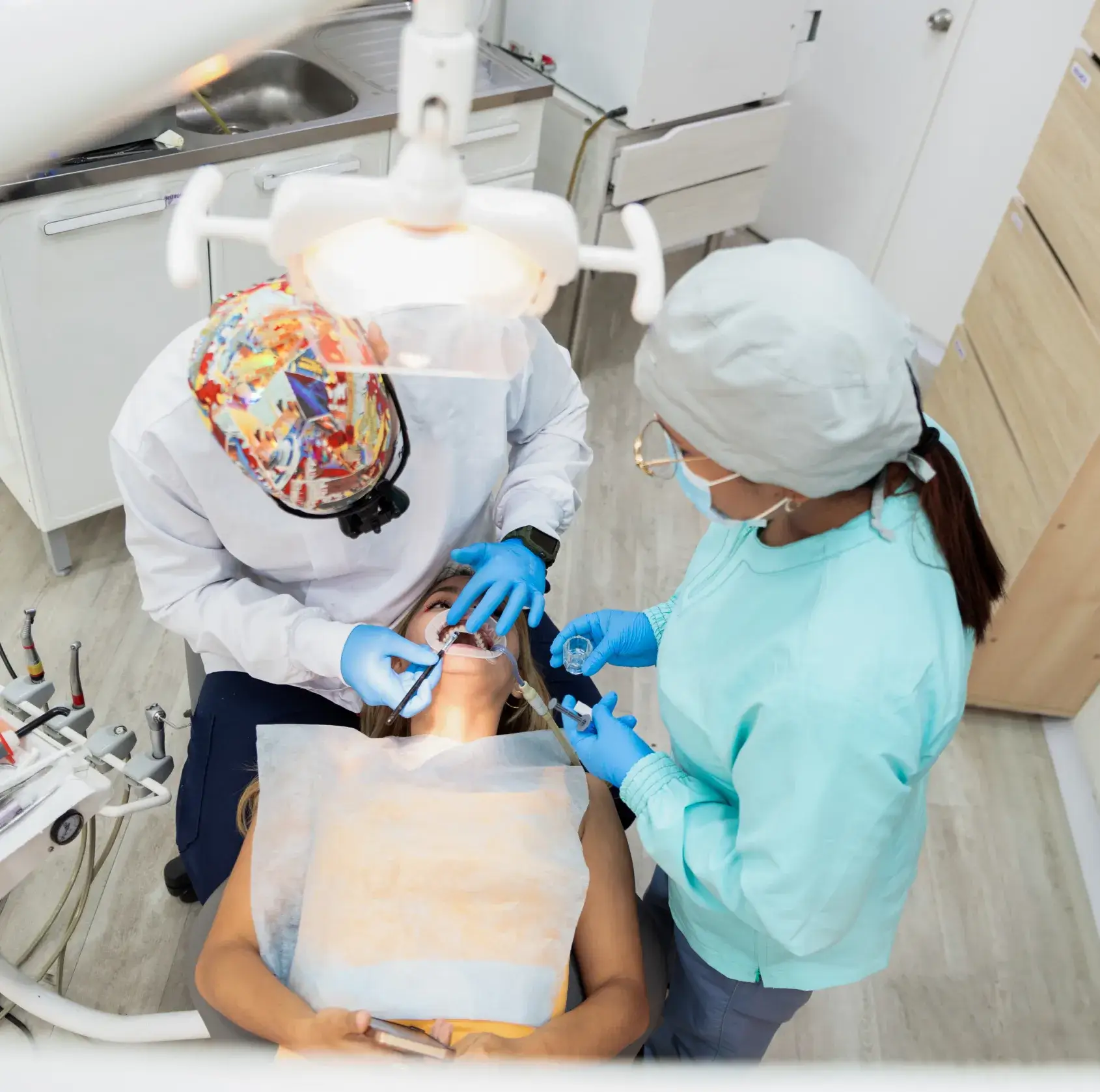 Dentist and dental assistant wearing protective gear performing a dental procedure on a patient reclining in a dental chair.