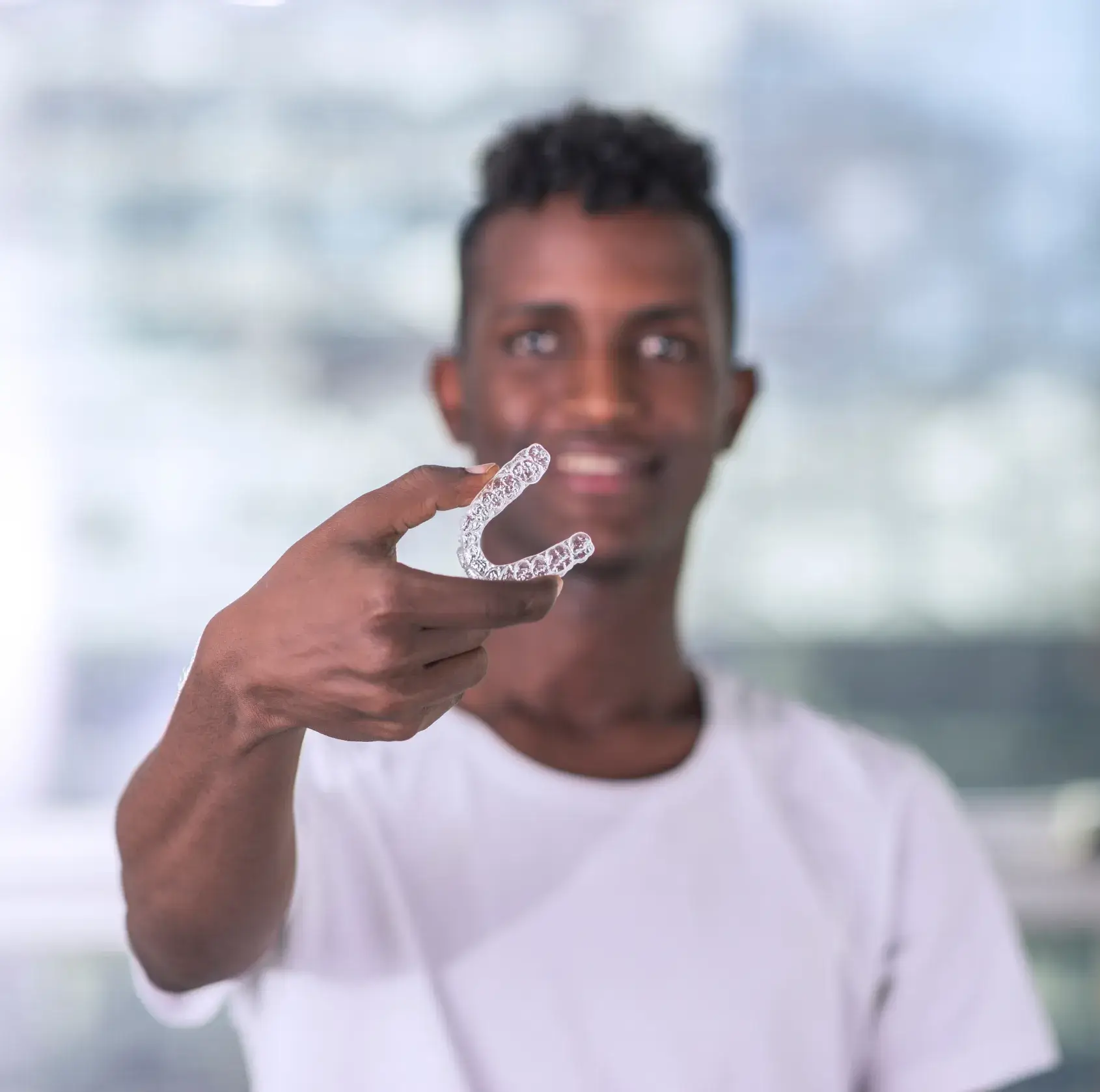 Smiling man holding a clear dental aligner towards the camera.