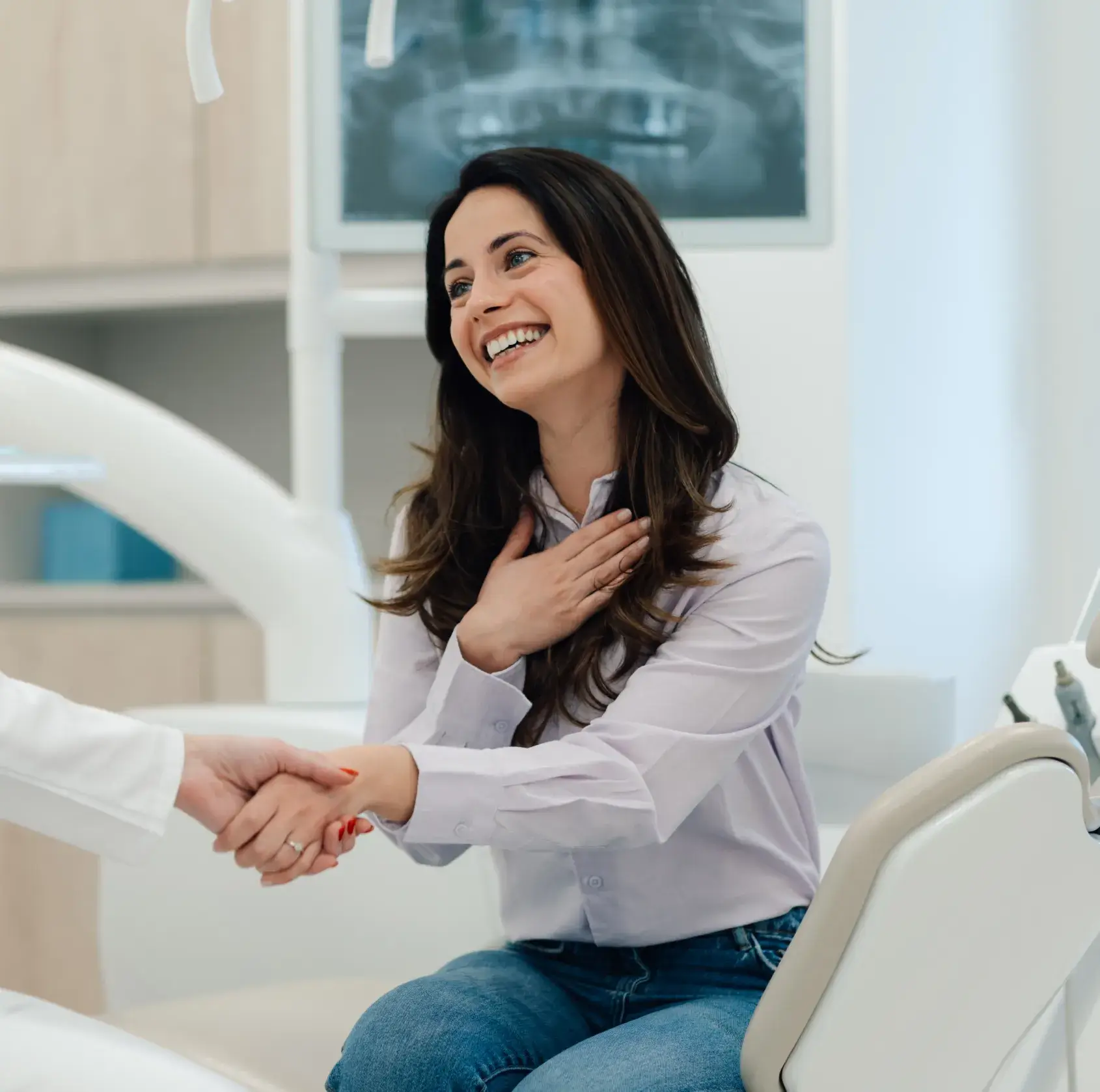 Smiling woman sitting in a dental chair shaking hands with a dentist in a clinic.