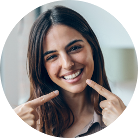Smiling young woman with long brown hair pointing to her teeth.