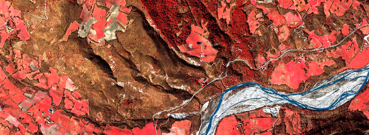 False-color satellite image showing a river flowing through red and brown agricultural and forested land.