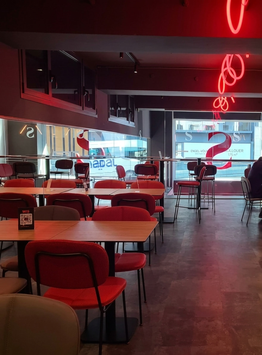 Interior d'un restaurant modern amb cadiretes vermelles, taules de fusta i il·luminació de neó vermella.