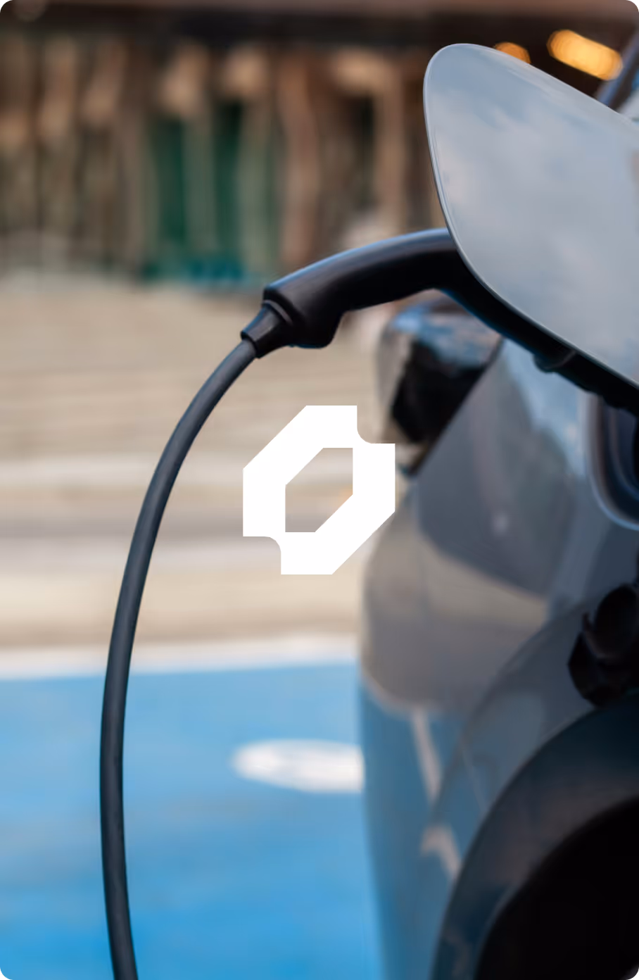 Electric car being charged at a charging station with a black charging cable connected to the vehicle.
