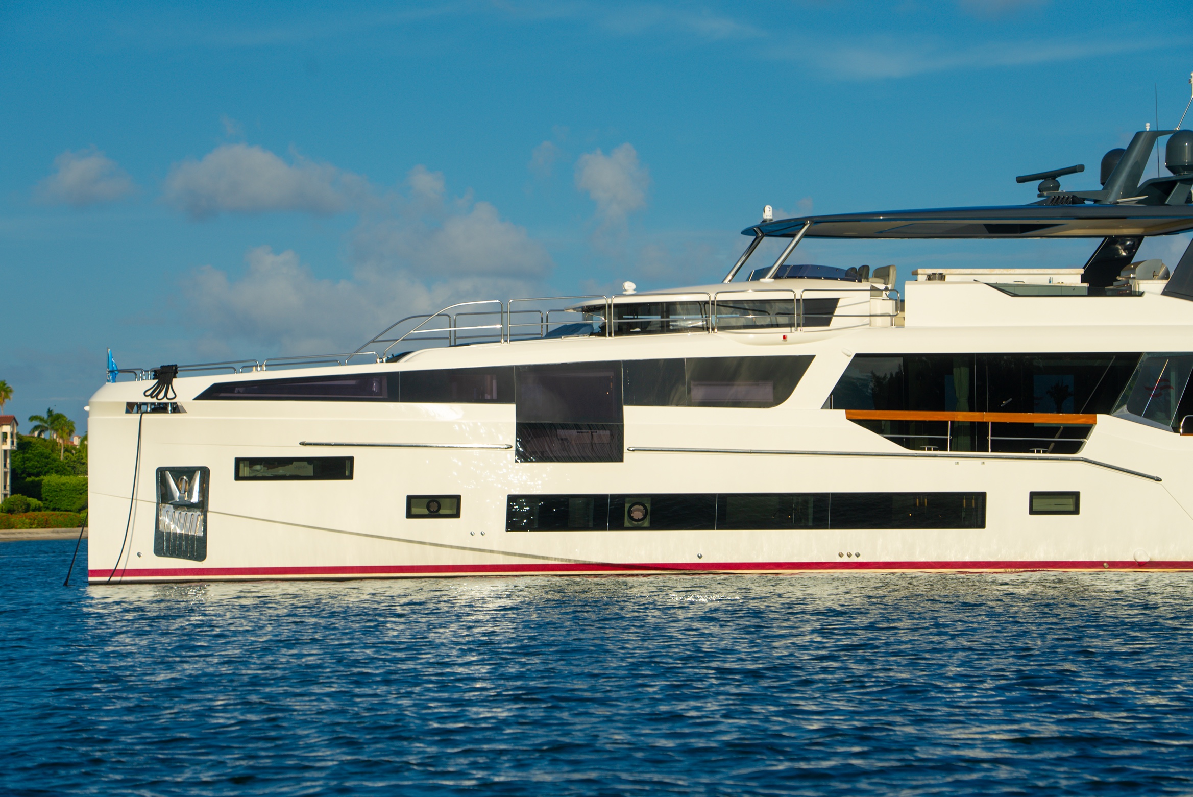 Side view of a white luxury yacht on calm blue water under a partly cloudy sky.