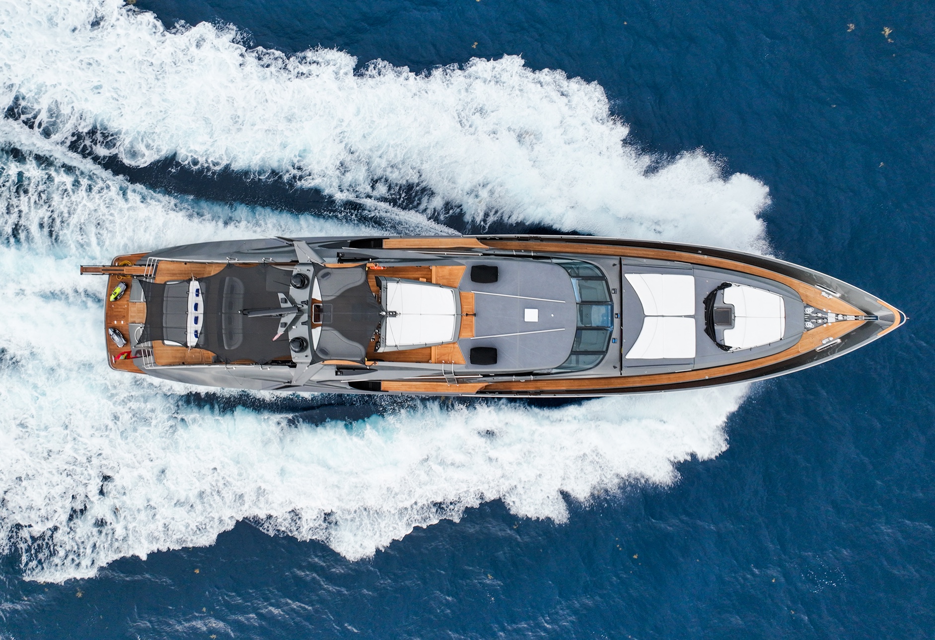 A luxury yacht cruising through deep blue water, creating white foamy waves.