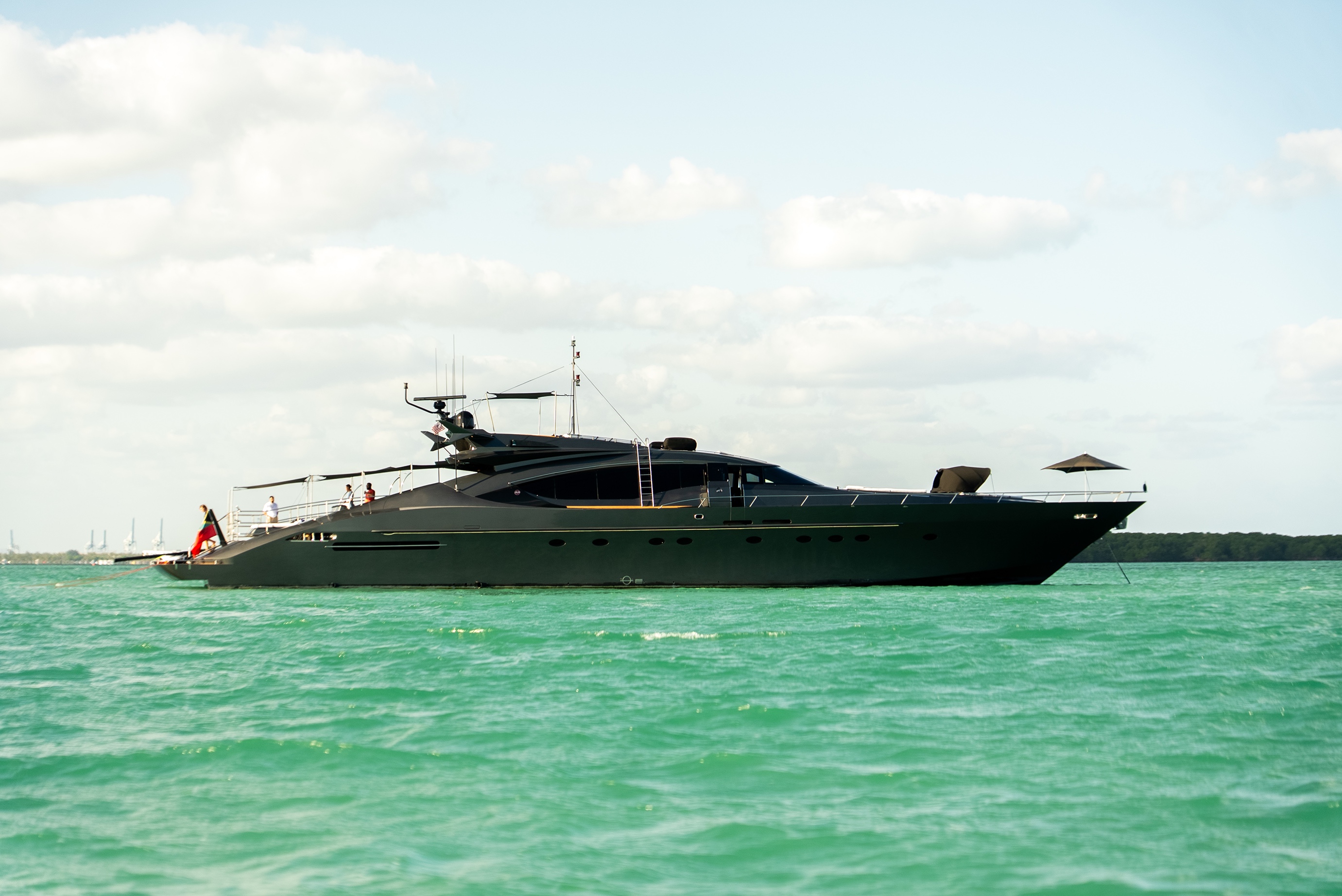 Sleek black luxury yacht floating on turquoise water under a partly cloudy sky.