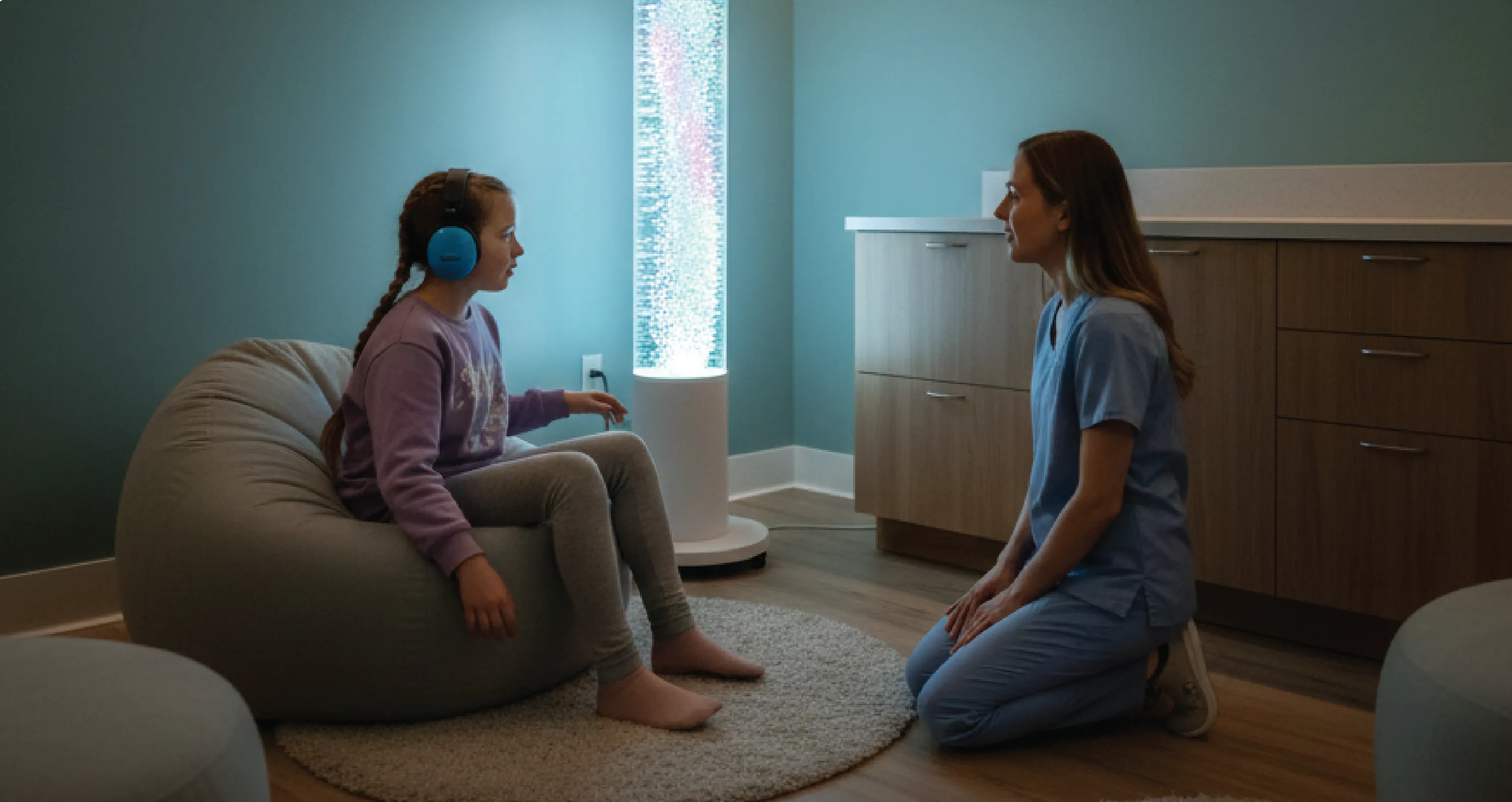 Girl with blue headphones sitting on beanbag talking to healthcare professional