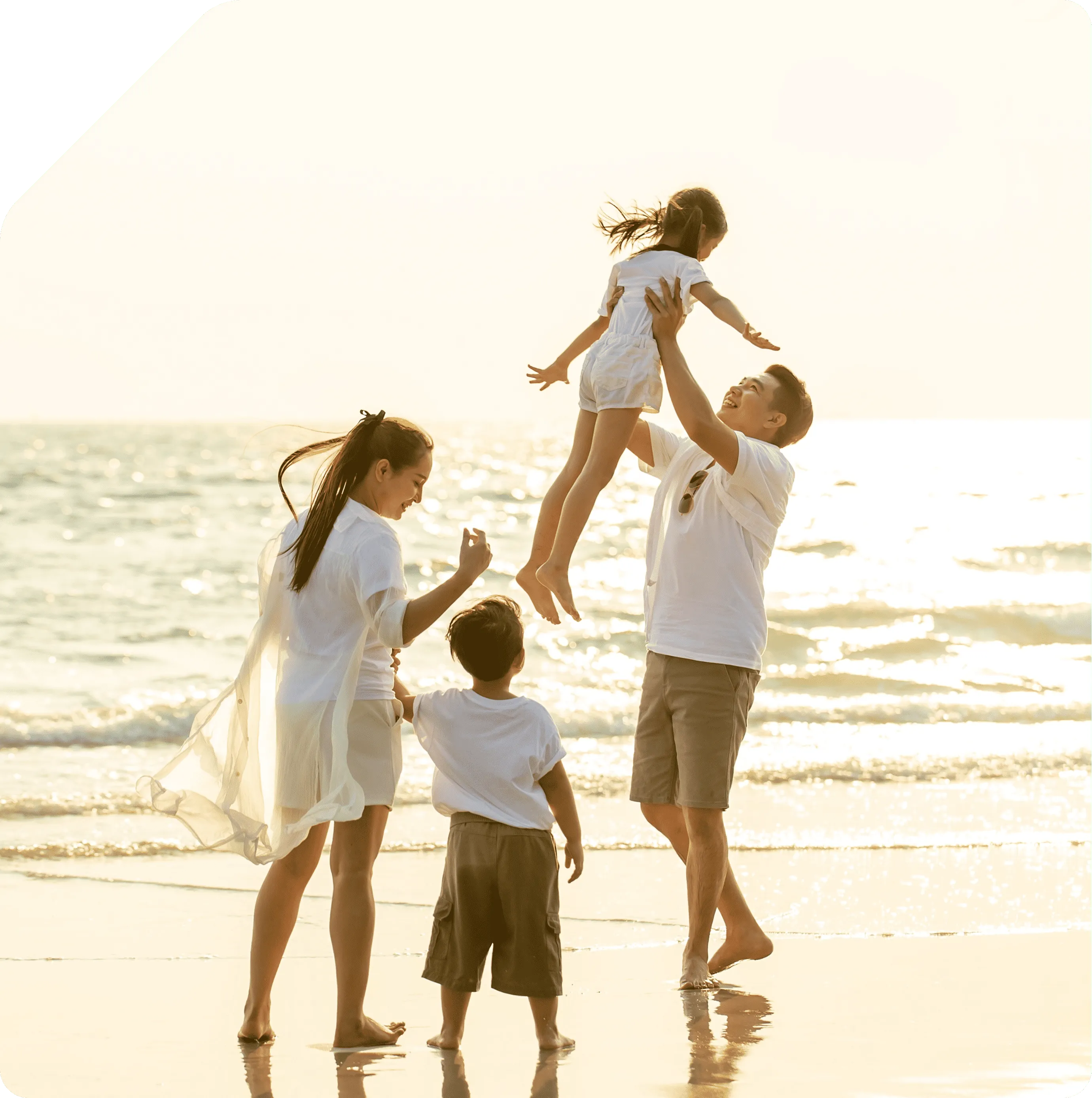 Family playing together on beach at sunset, lifting child in air