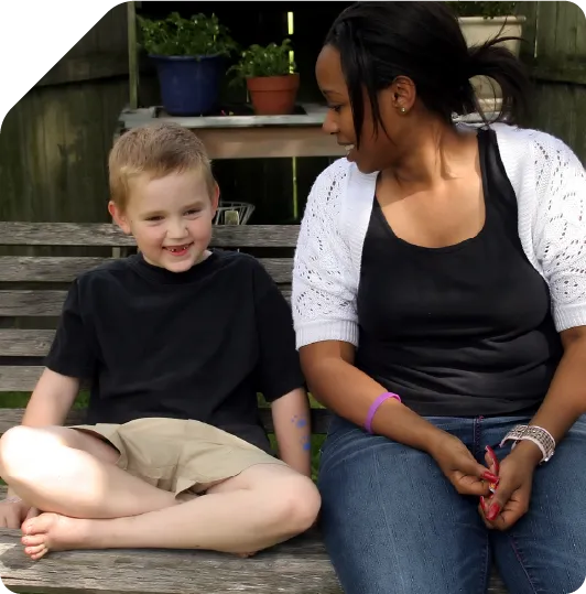 Smiling child and caregiver sitting together on wooden bench outdoors