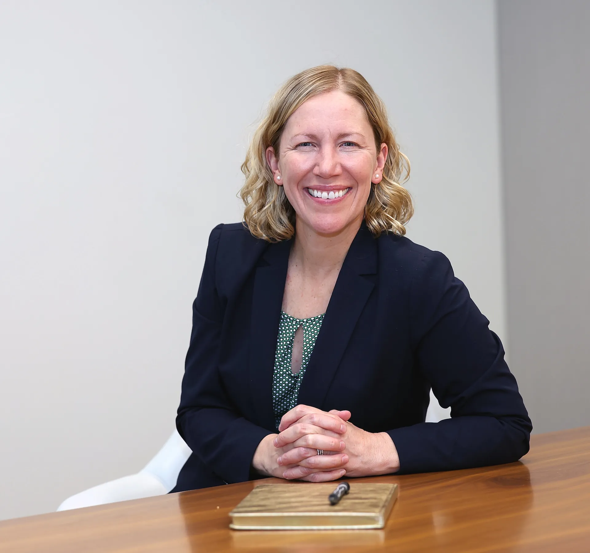 Professional woman smiling at desk in navy blazer and green top