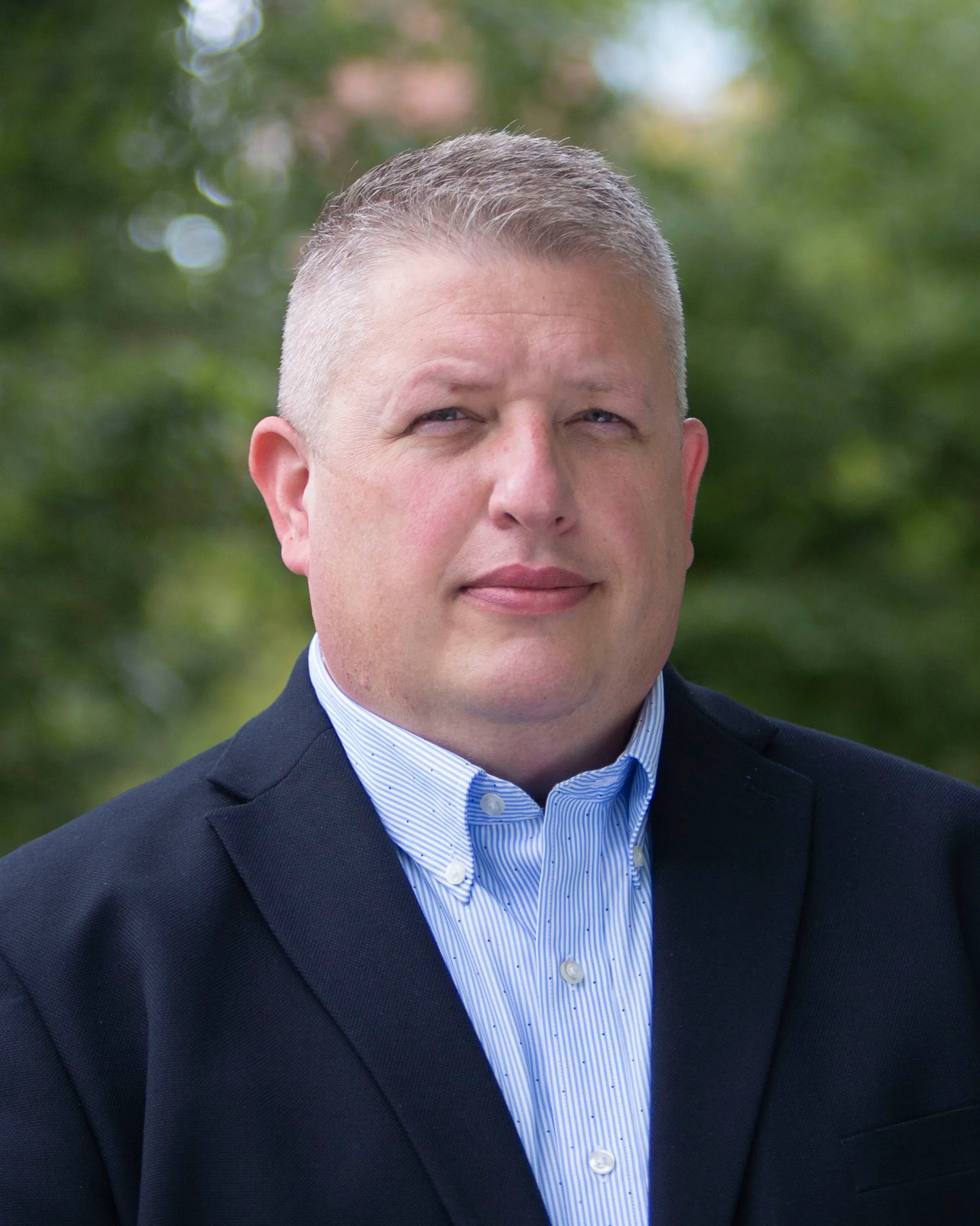 Professional headshot of a man in a navy suit and blue striped shirt