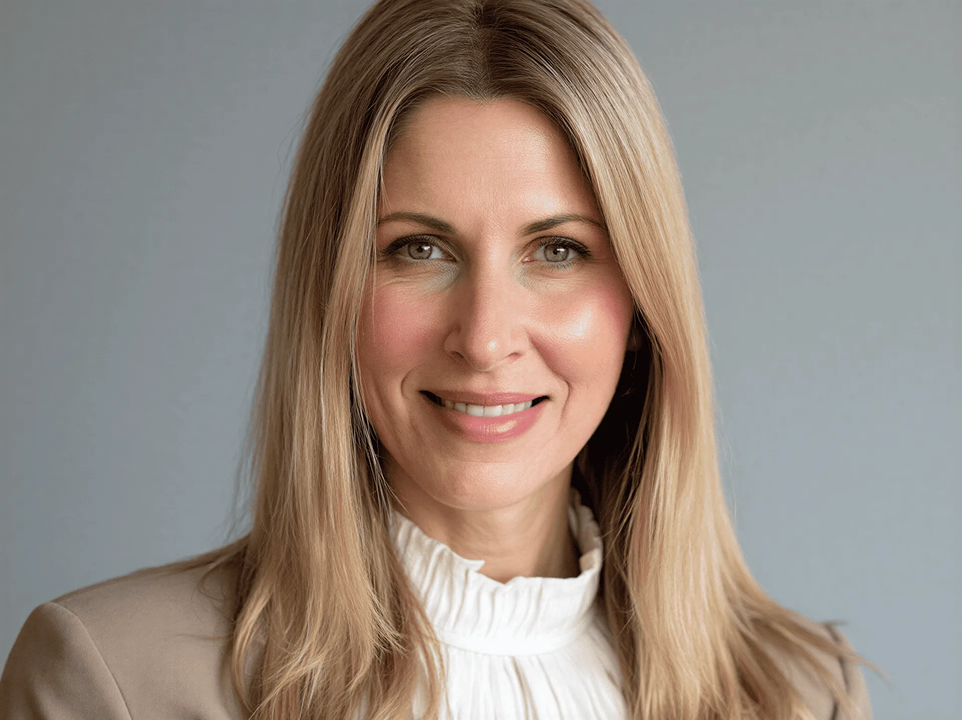 Smiling woman with blonde hair in white top against neutral background