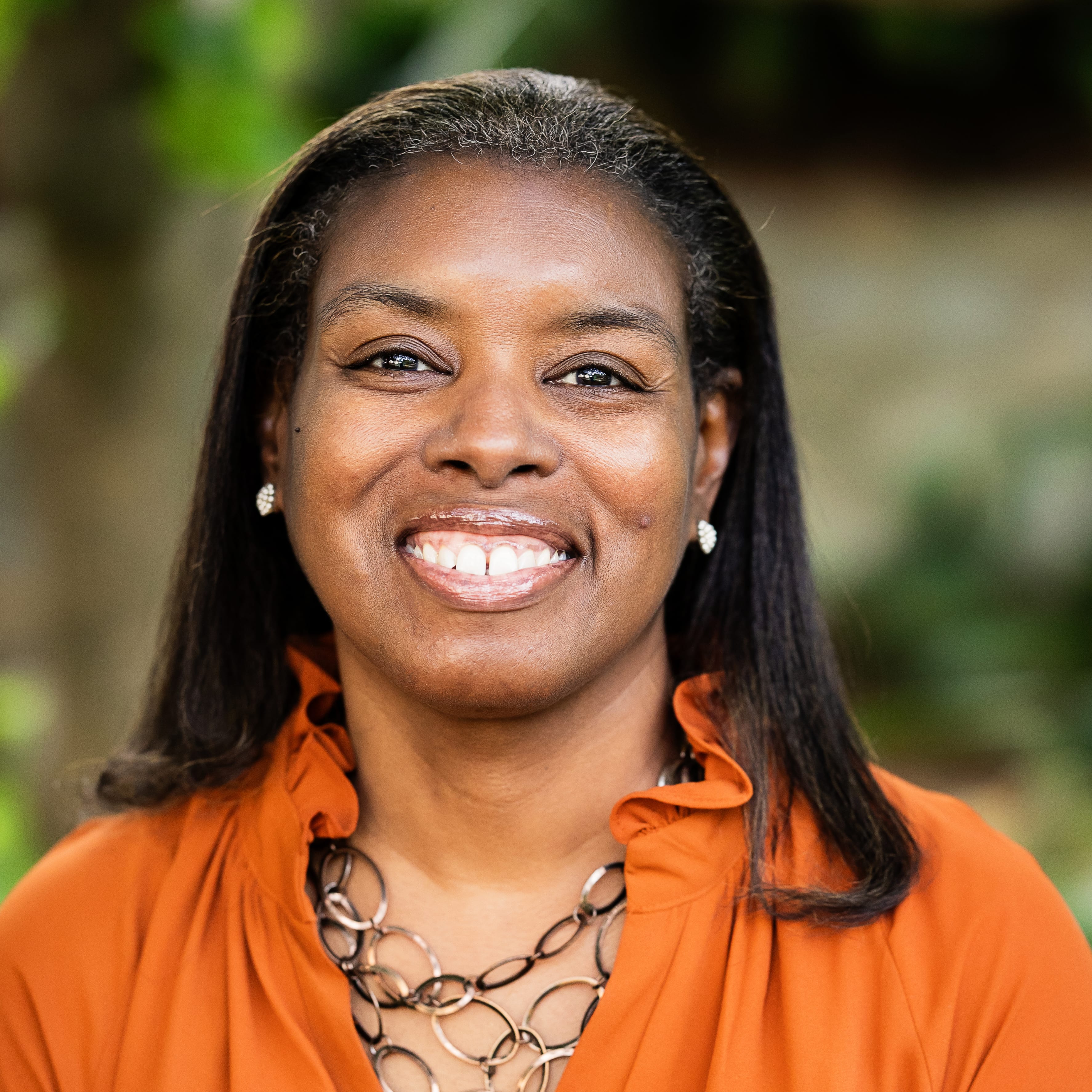 Woman in orange blouse smiling warmly with blurred green background