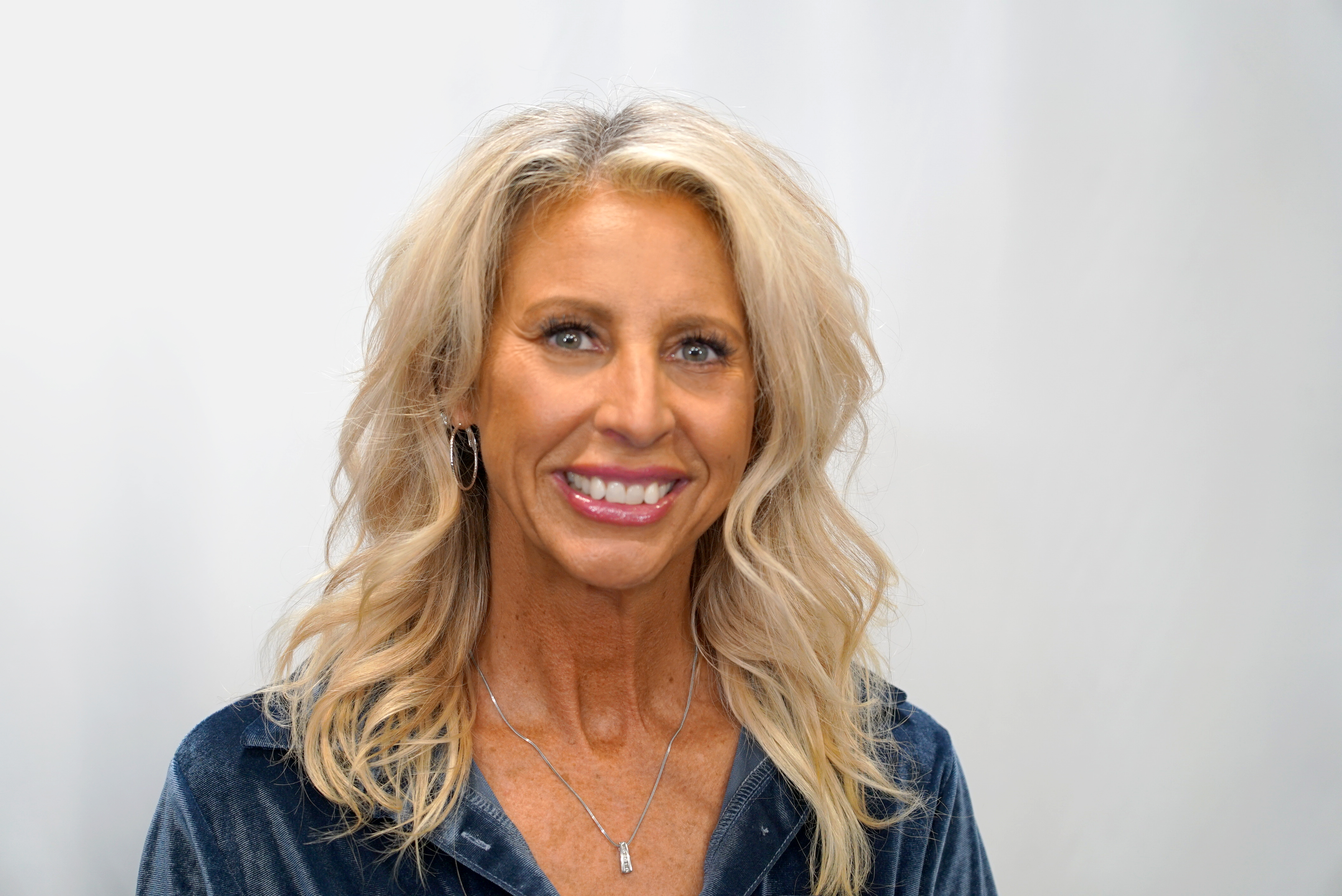 Blonde woman in blue jacket smiling warmly at camera
