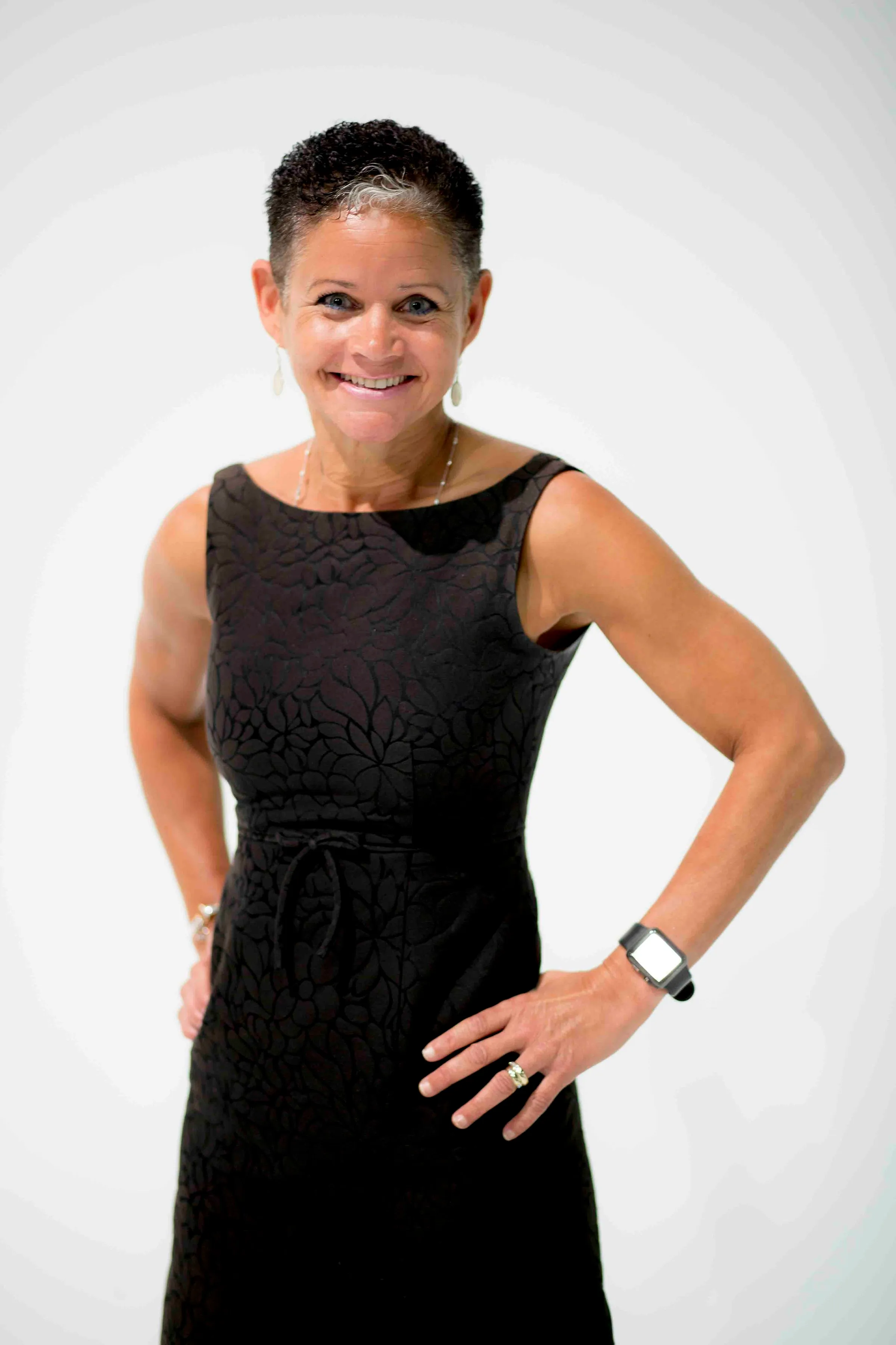 Smiling woman in black textured dress posing confidently against white background