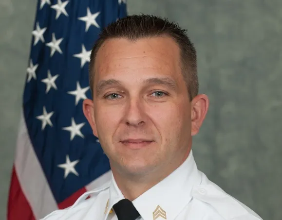 Military service member in white uniform standing in front of American flag