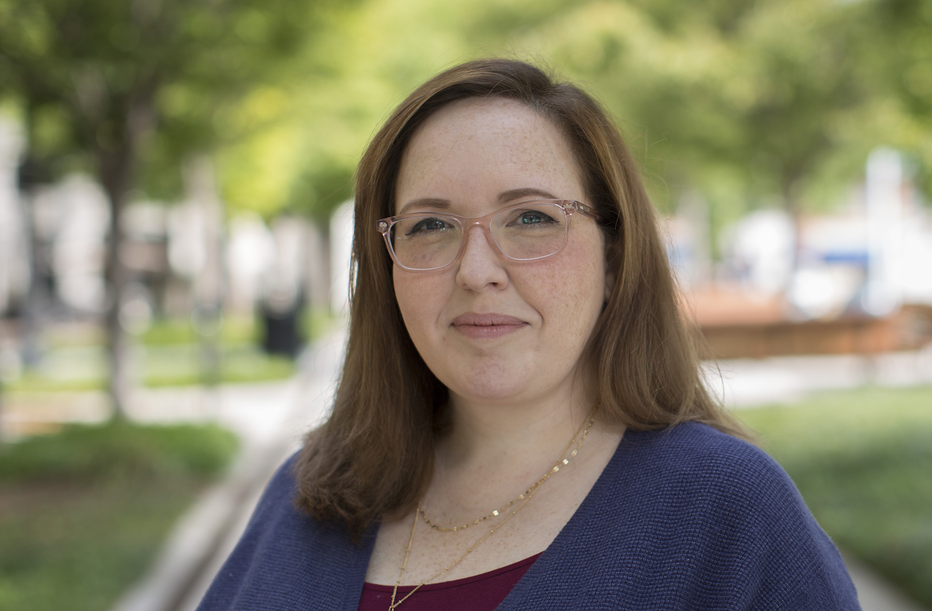 Woman with glasses smiling outdoors in a blue cardigan