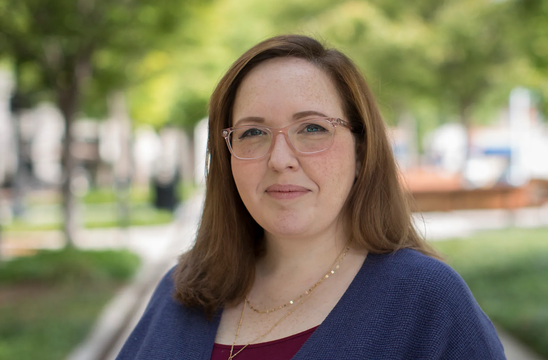 Woman with glasses smiling outdoors in a blue cardigan