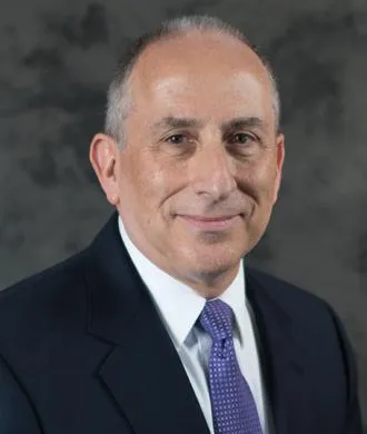 Older professional man in suit and purple tie smiling at camera