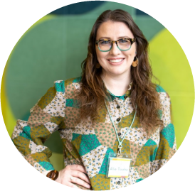 Smiling woman in glasses wearing colorful patchwork-style blouse against green background
