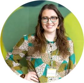 Smiling woman in glasses wearing colorful patchwork-style blouse against green background