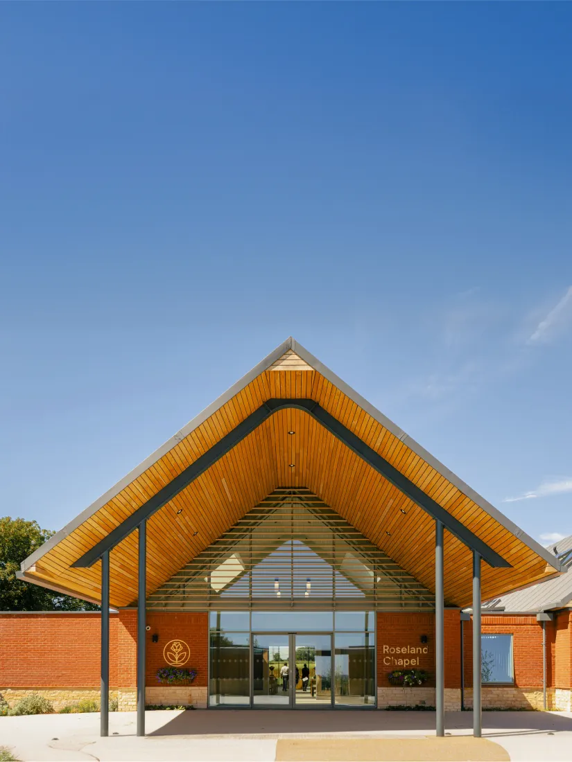 Front entrance of Roseland Chapel with a wooden peaked roof and glass doors under a blue sky.