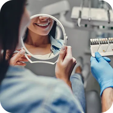 Patient smiling while looking at her teeth reflection in a round mirror during a dental shade matching with a dentist.