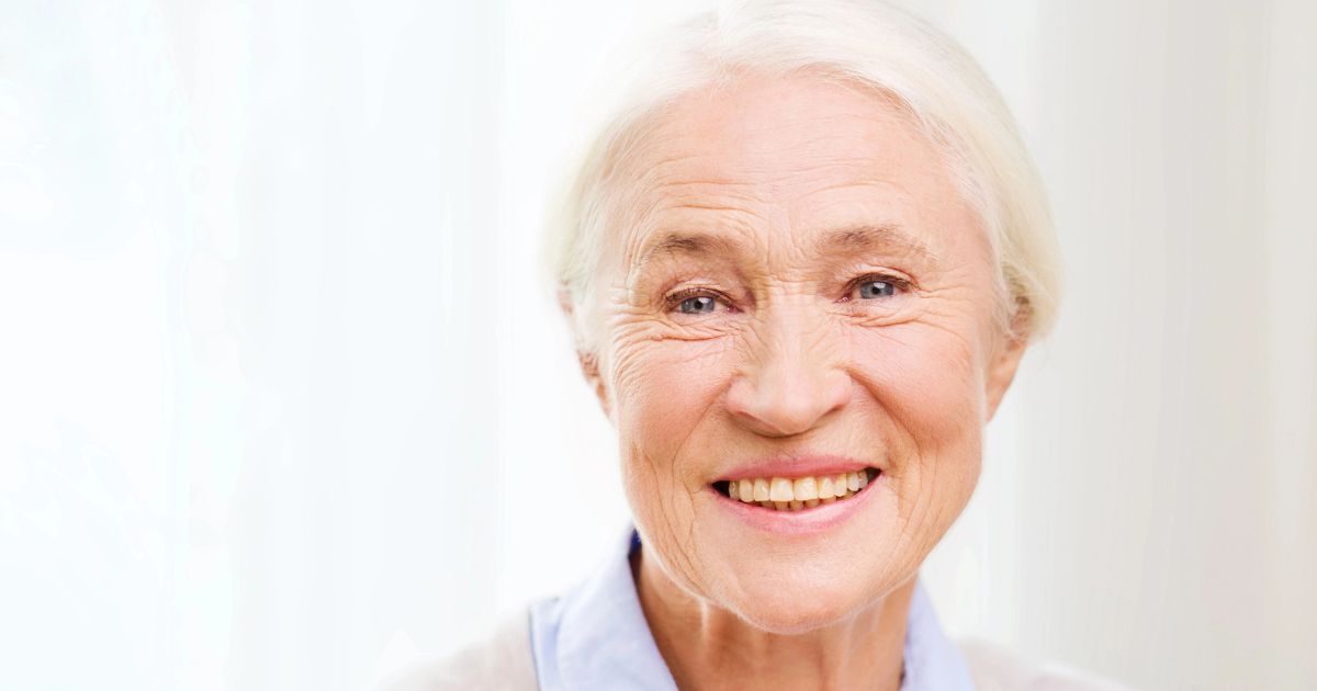 Smiling elderly woman with white hair and blue eyes wearing a light blue collared shirt.