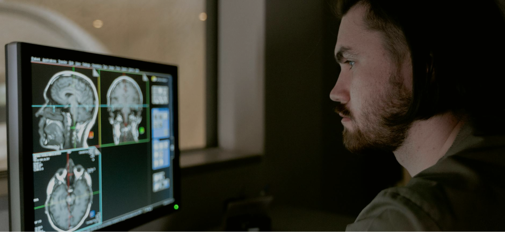 Grayscale image of a radiologist looking at medical imaging scans on a large monitor.
