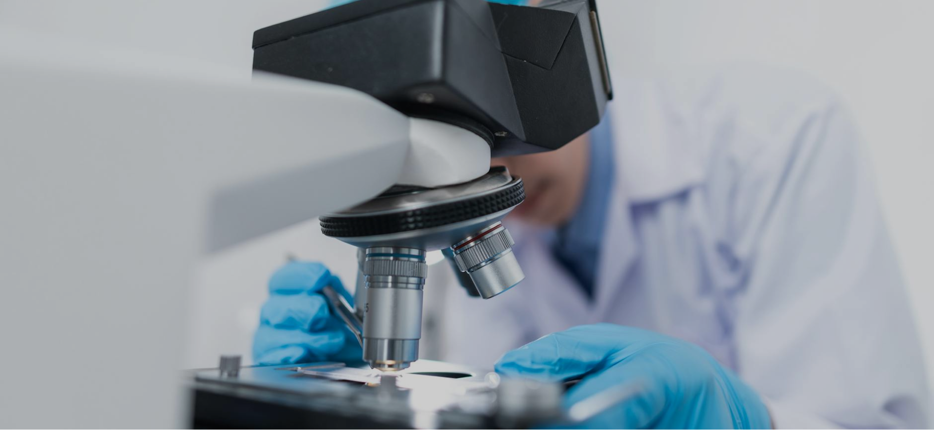Grayscale image of a laboratory professional looking through a microscope.