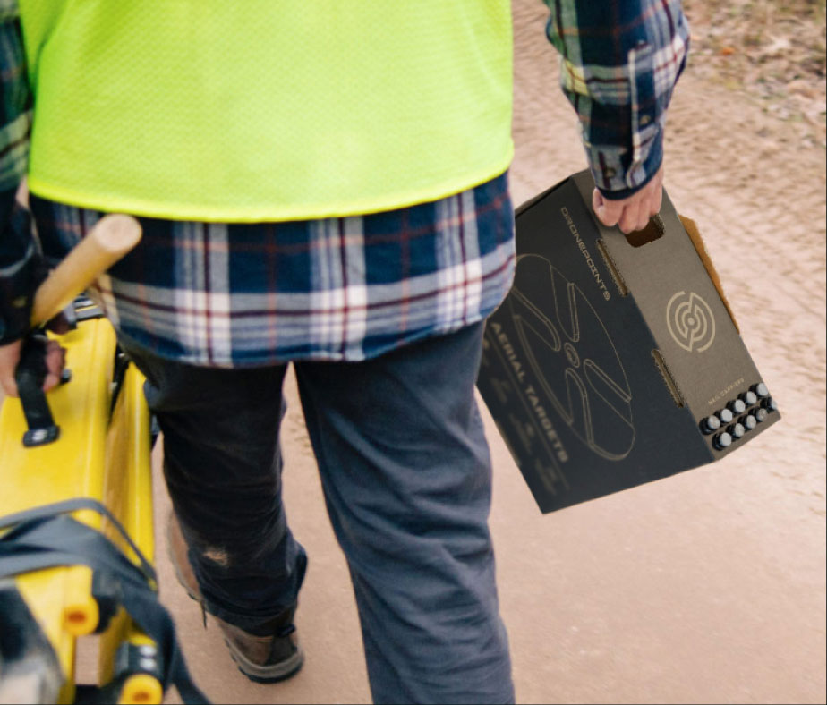A man carrying the DronePoints box along with his surveying gear