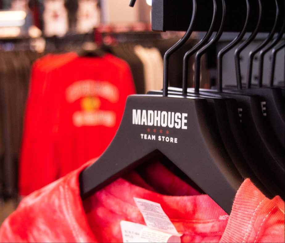 A photo of the Madhouse Team Store logo on a hanger with store merch hanging from it