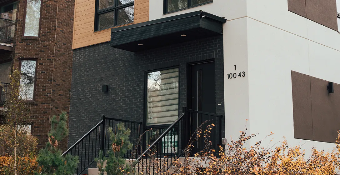Modern residential building entrance with black door, black brick wall, large window, and plants in front.