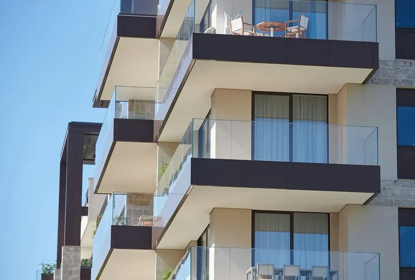 Modern apartment building with multiple glass balconies and outdoor furniture under clear blue sky.