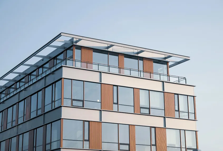 Modern building facade with large glass windows and vertical wooden panels under a clear sky.