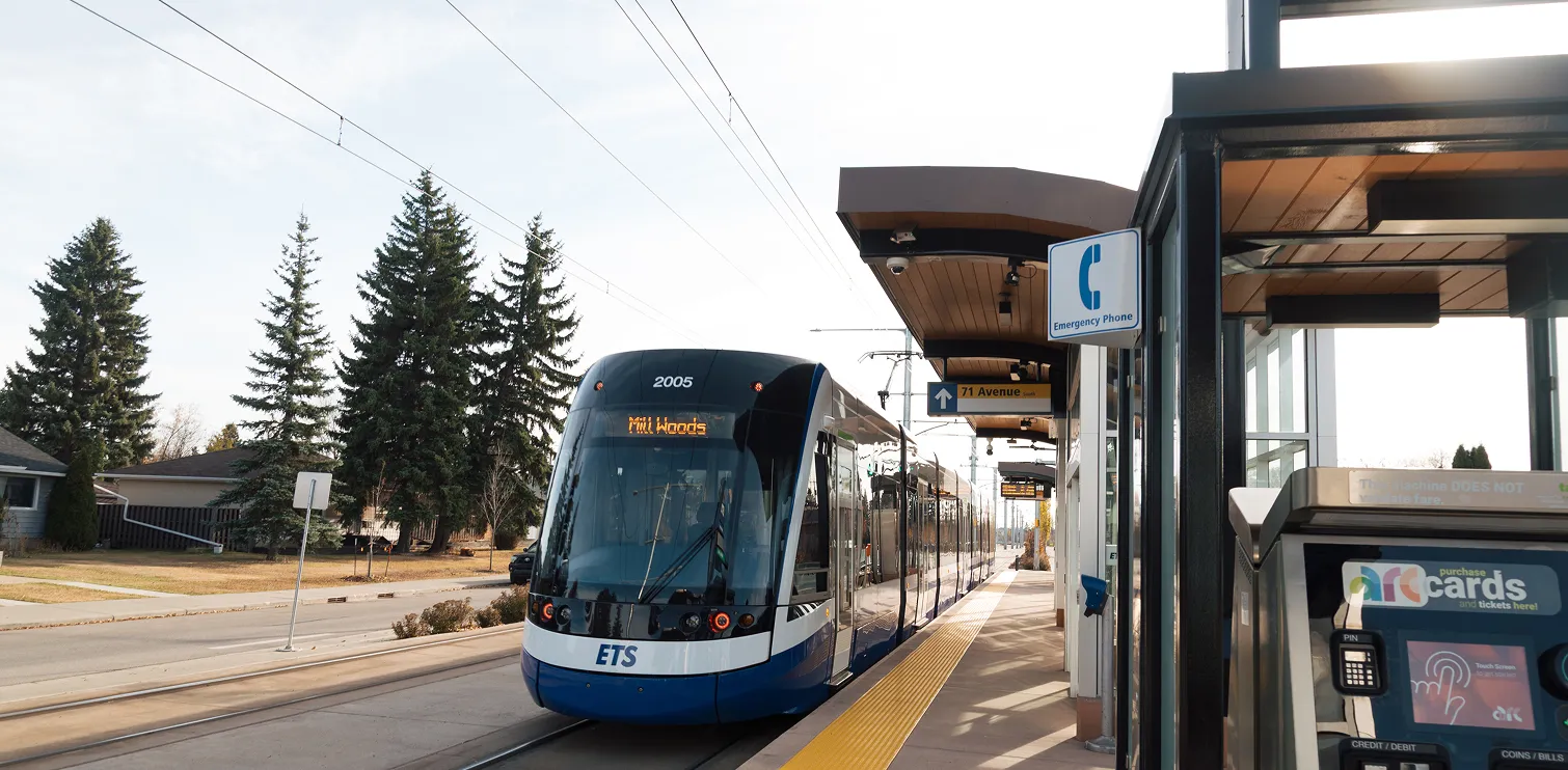 Modern light rail train numbered 2005 stopped at a station platform with an emergency phone sign and ticket machine visible.
