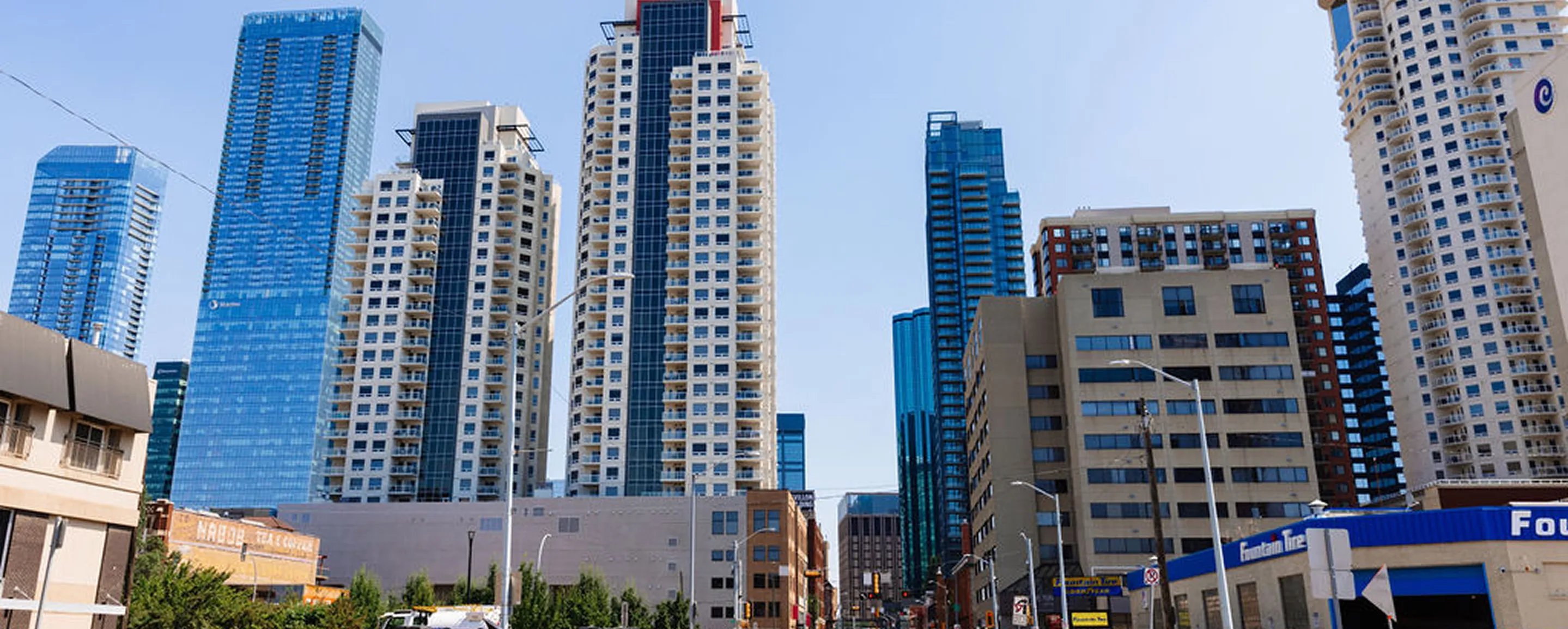 Downtown city street with tall modern skyscrapers and buildings under a clear blue sky.