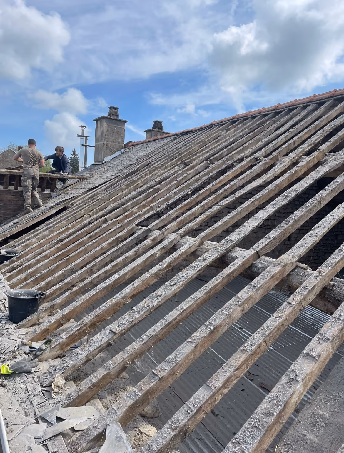 Ancienne charpente, chevrons noirs, bois humide, lumière naturelle faible, structure vieillie à Chéhéry.
