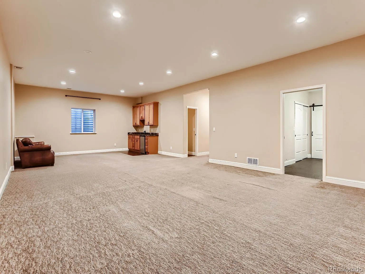 Spacious finished basement with recessed lighting, neutral carpeting, and built-in kitchenette, designed and completed by Denver Dream Builders.